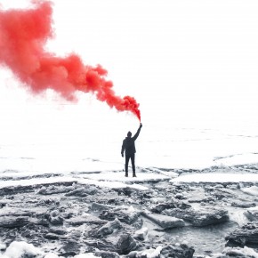 Silhouette einer Person von hinten, in schwarz-weiß, die ein rotes Rauchsignal hält