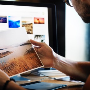 Mann betrachtet Ausdruck eines Fotos vor einem Monitor mit weiteren Fotos